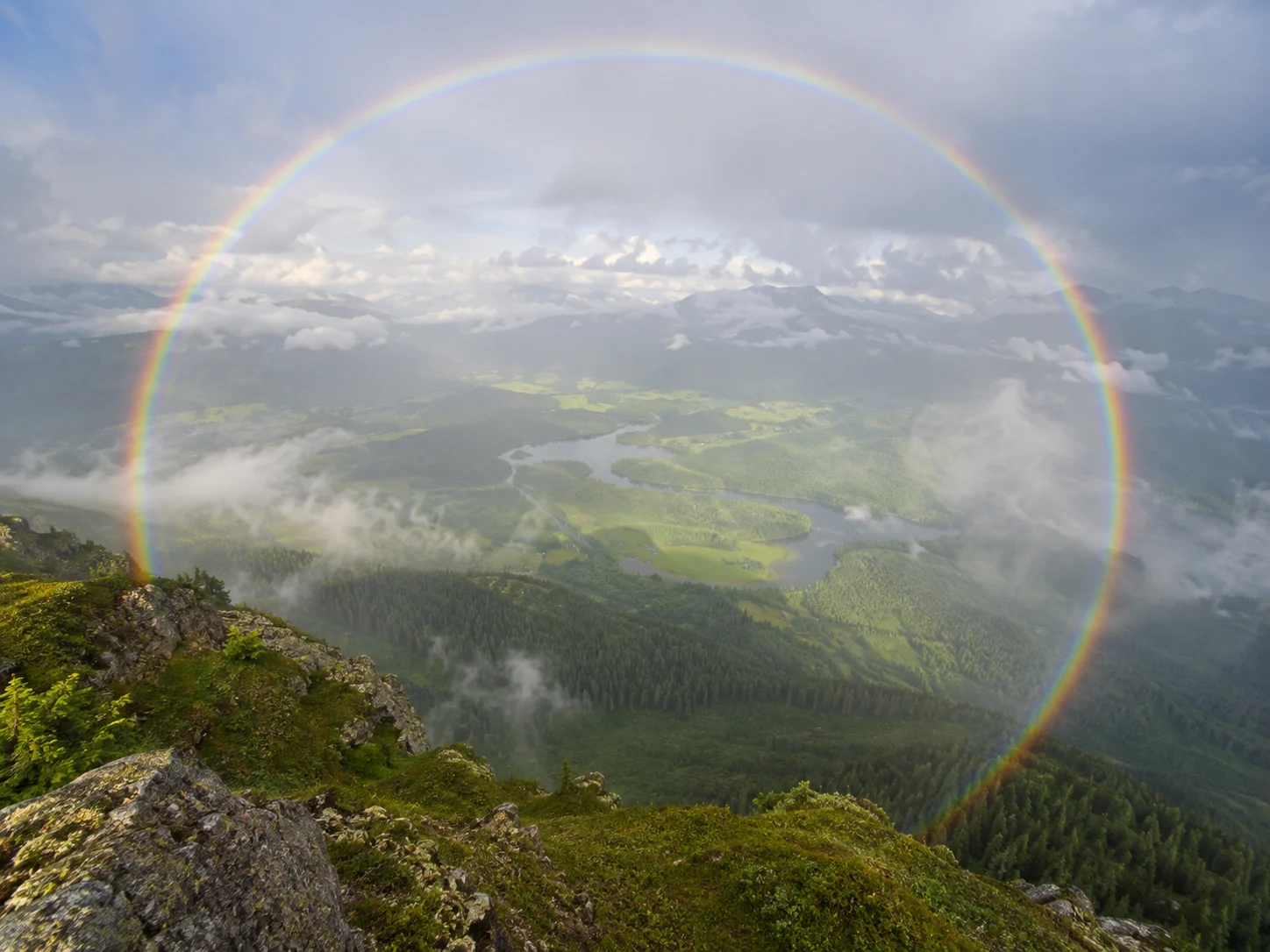 A complete circular rainbow above a misty green valley
