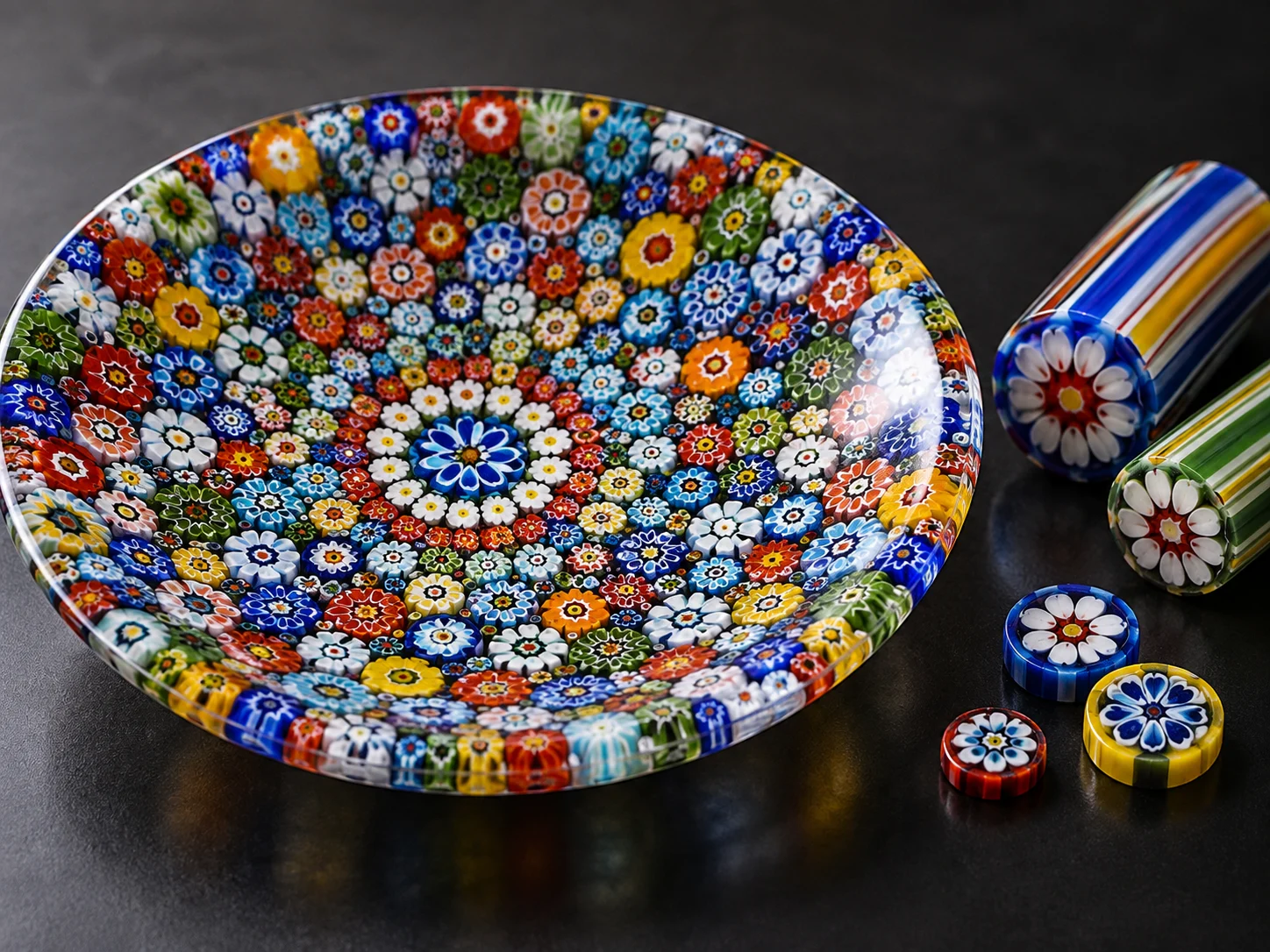A colorful millefiori glass plate beside patterned glass canes and slices