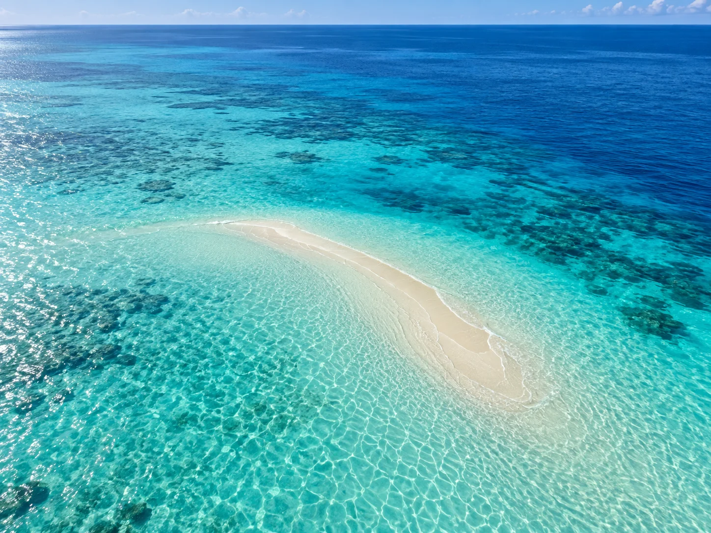 Clear ocean water changing from turquoise over sand to deep cobalt blue