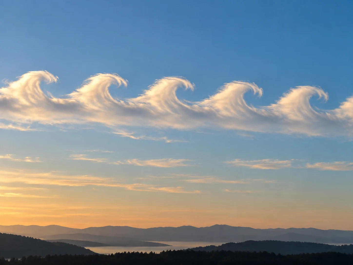 A neat row of white clouds curling like breaking ocean waves in a blue sky