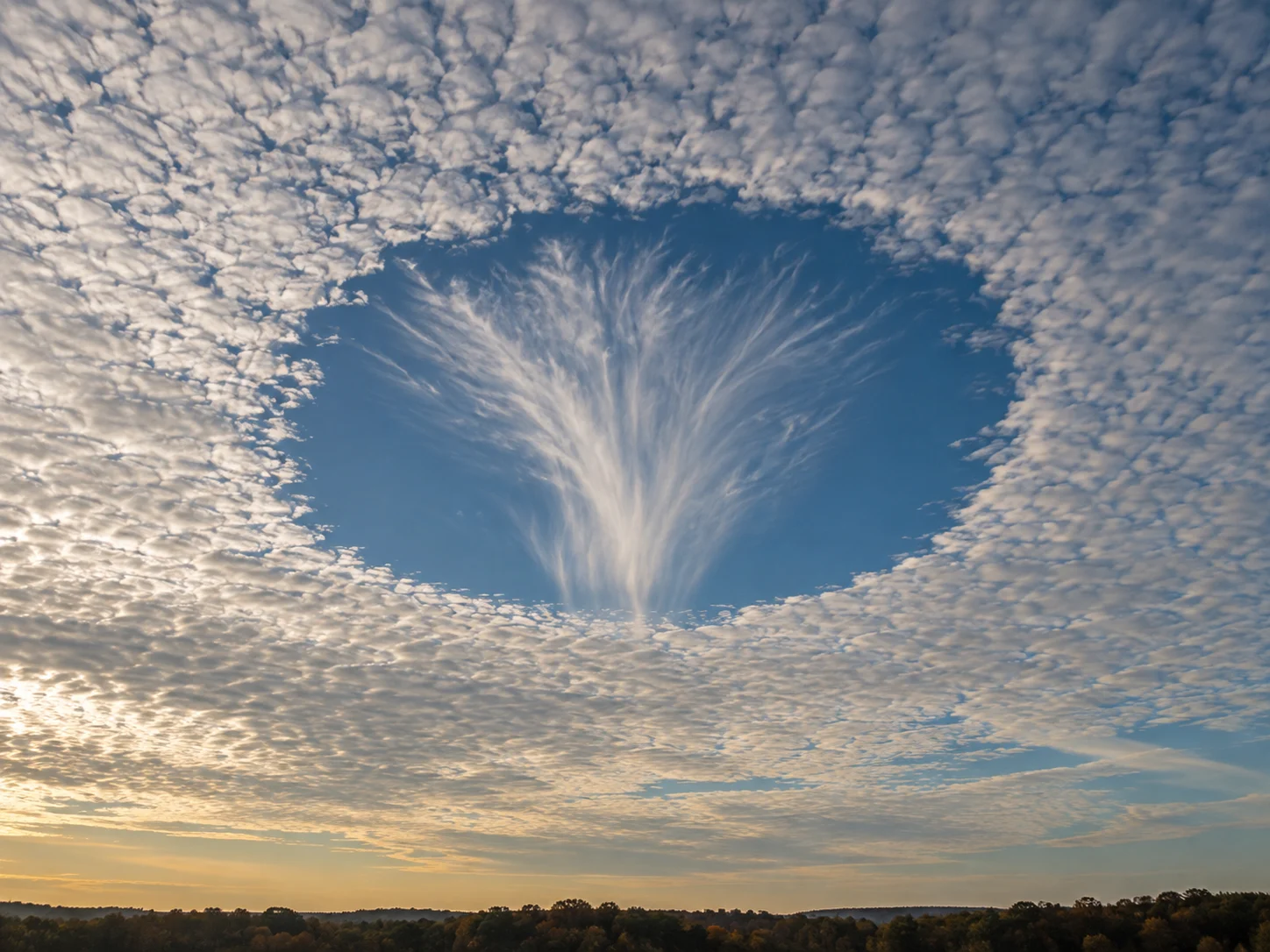 A large round opening in a thin cloud sheet with feathery ice falling from its center