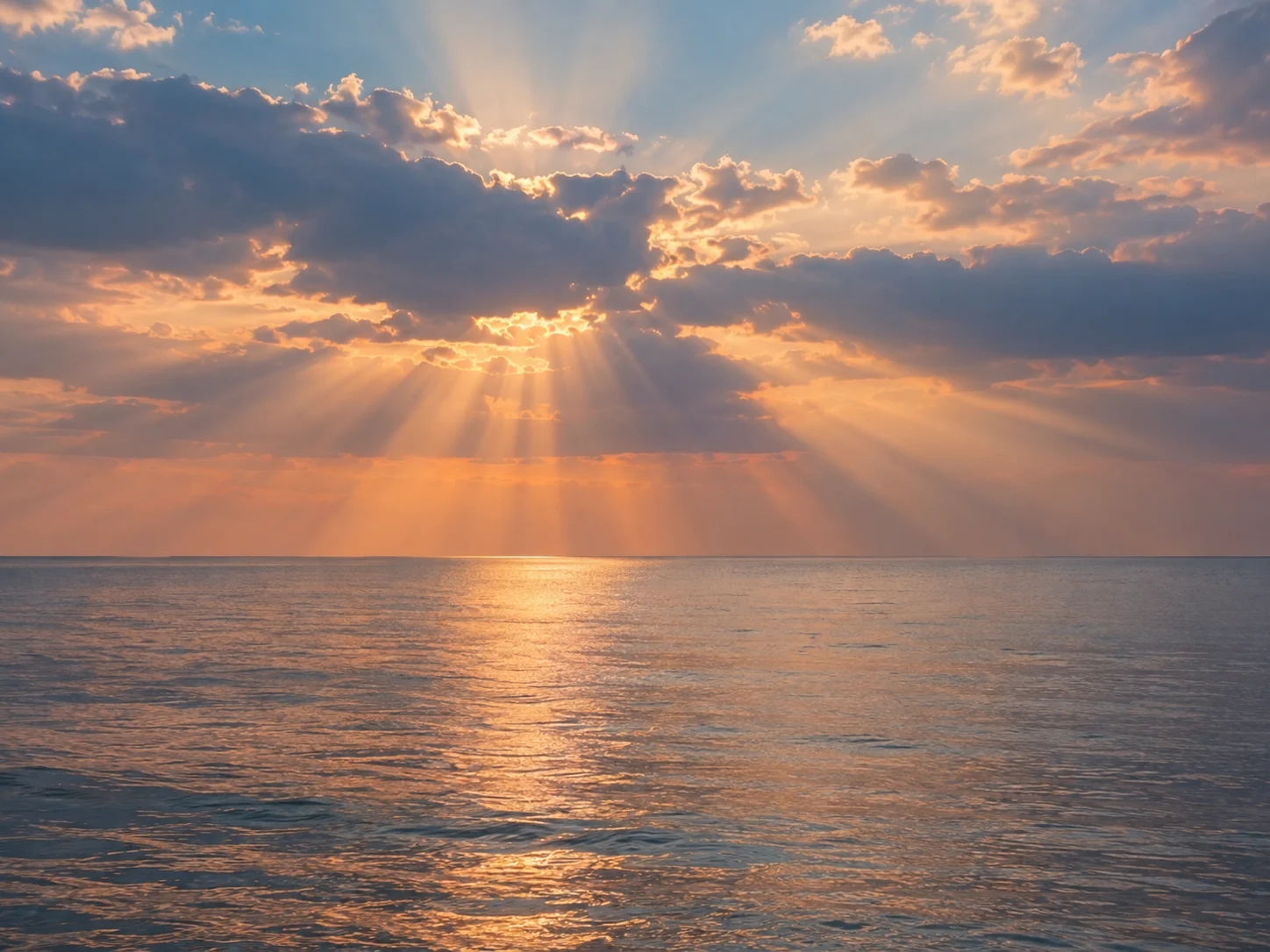 Warm sunbeams appearing to fan through cloud gaps over a calm sea