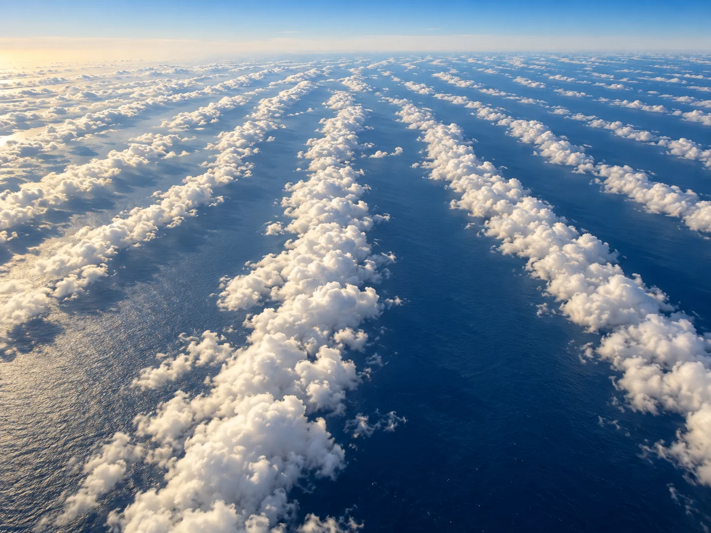 Long parallel rows of white cumulus clouds stretching over a deep blue ocean