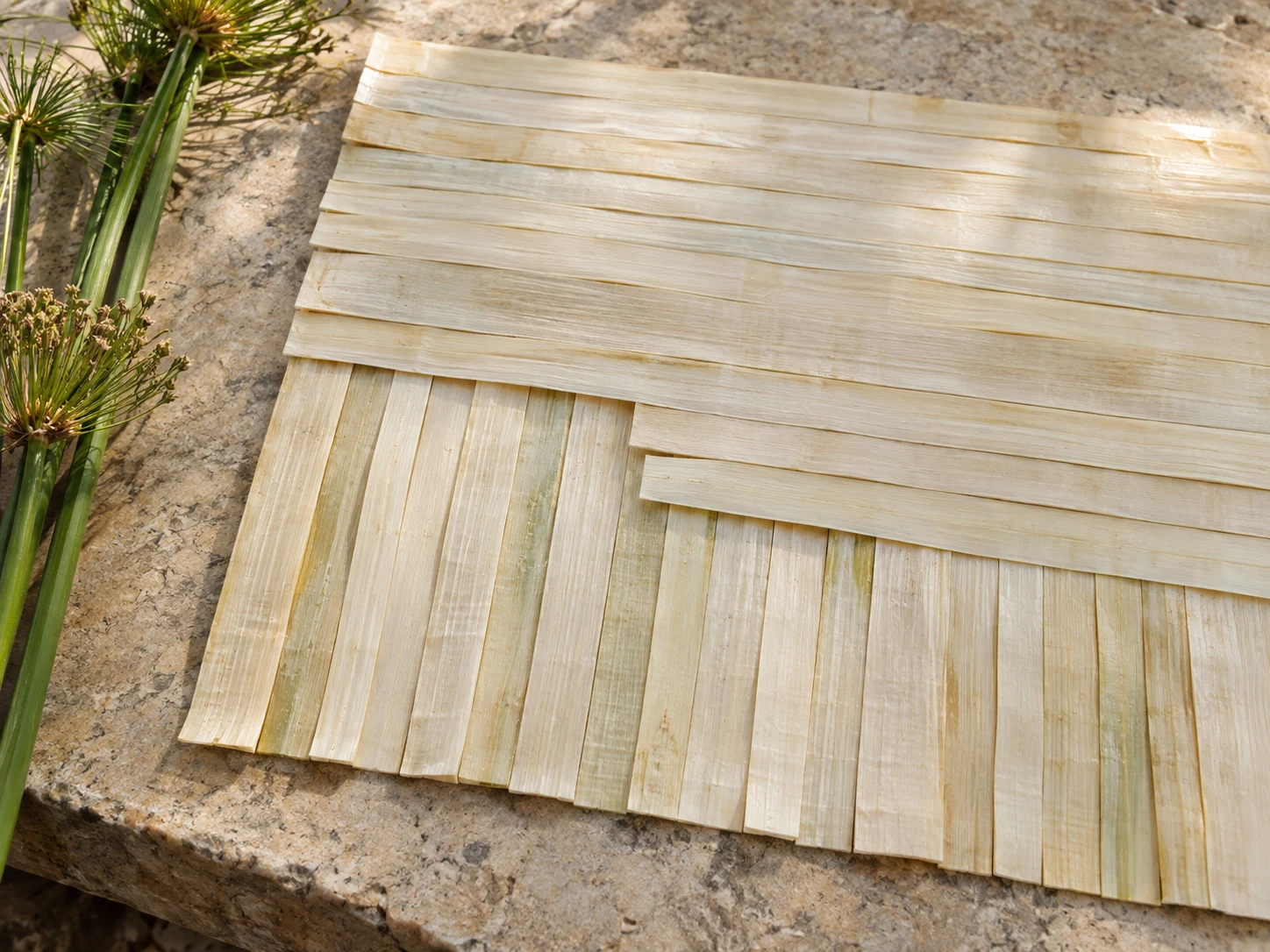 Two flat layers of pale papyrus strips laid across each other on a sunlit stone table