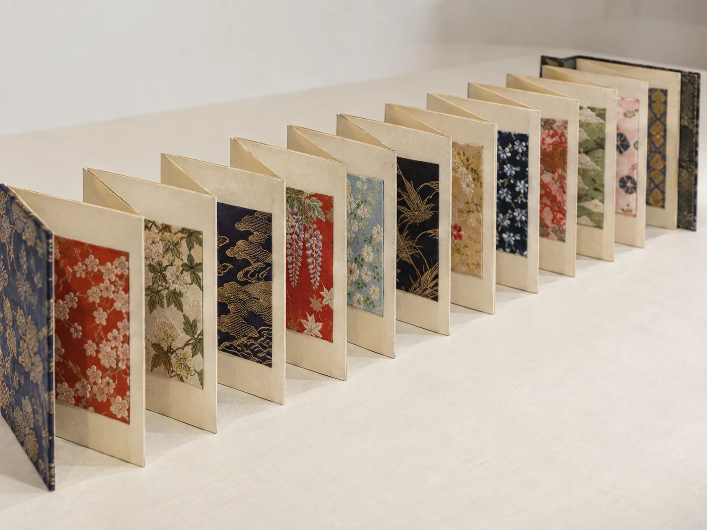 An accordion-fold album standing open with a different patterned silk sample on each page