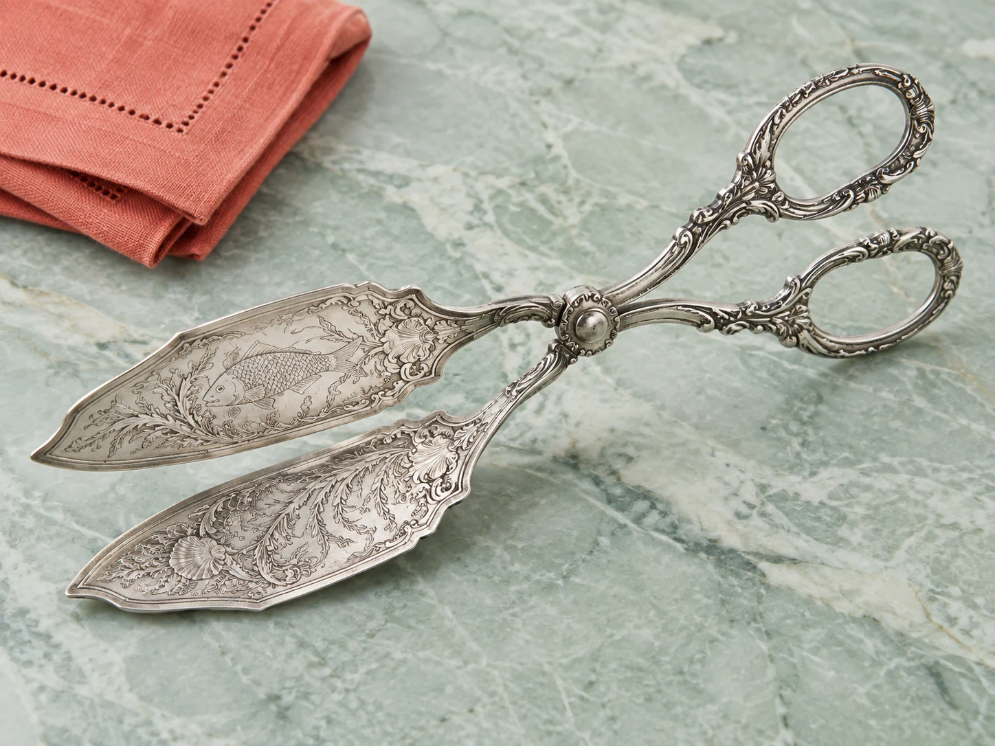 An ornate silver double-bladed fish server opened like broad engraved tongs